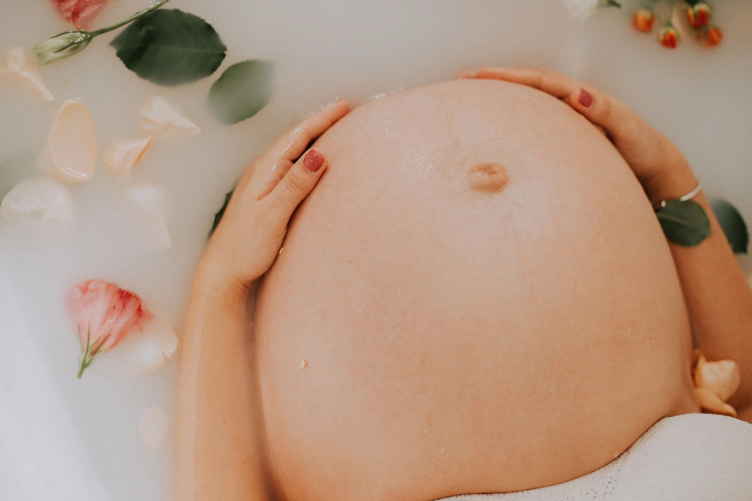 Bauch einer schwangeren Mutter mit Schilddrüsenunterfunktion in der Badewanne mit Rosenblättern
