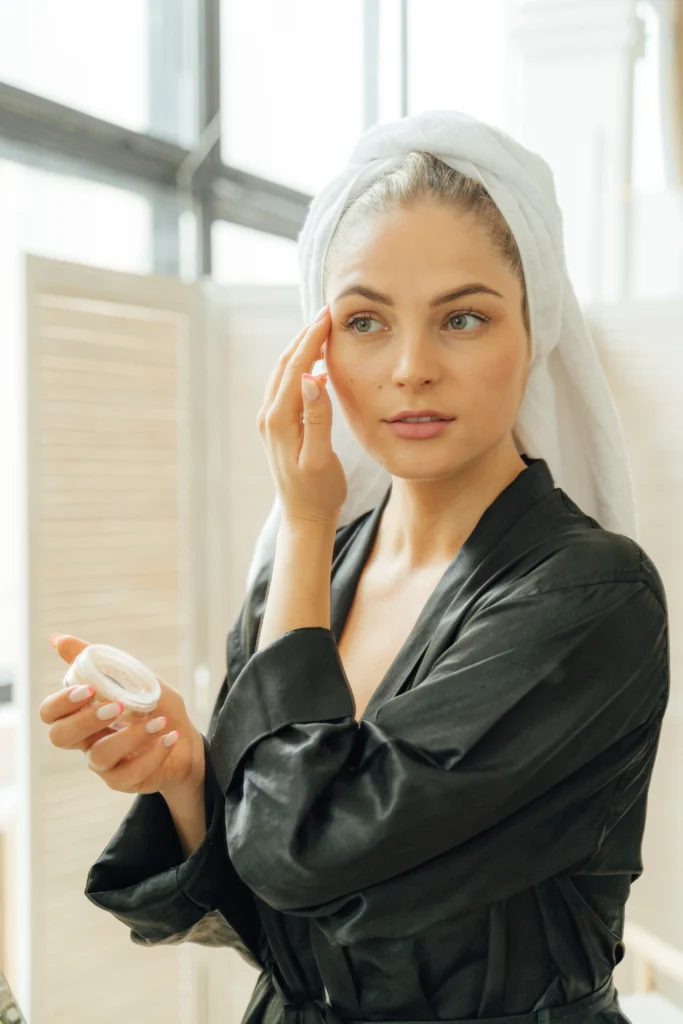 Kosmetik in der Schwangerschaft, Frau trägt Creme auf ihr Gesicht auf und trägt einen grauen Bademantel