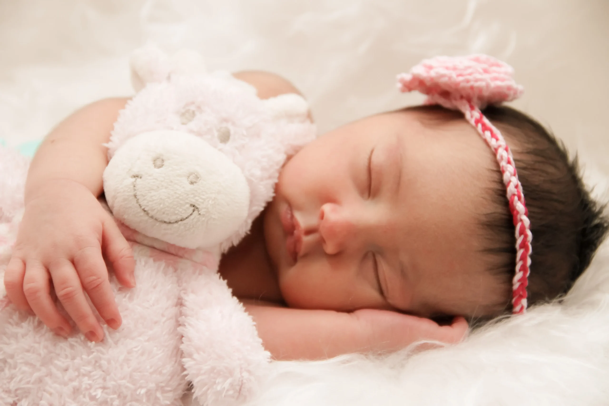 Beste Schlafposition in der Schwangerschaft, Baby schläft mit Teddy und rosa Haarband